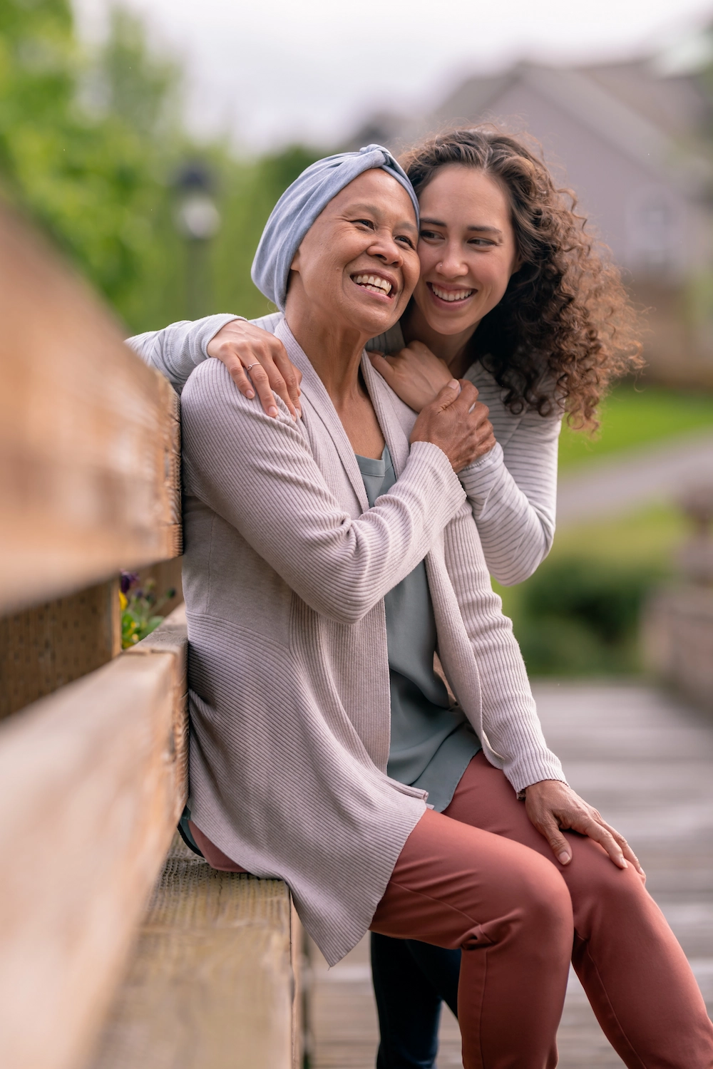 A senior woman with cancer is embraced and comforted by her adult daughter as they stand outside on a spring evening.