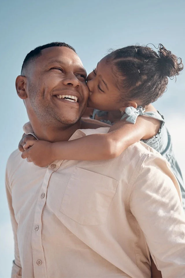 Smiling mixed race single father carrying little daughter on piggyback with copyspace