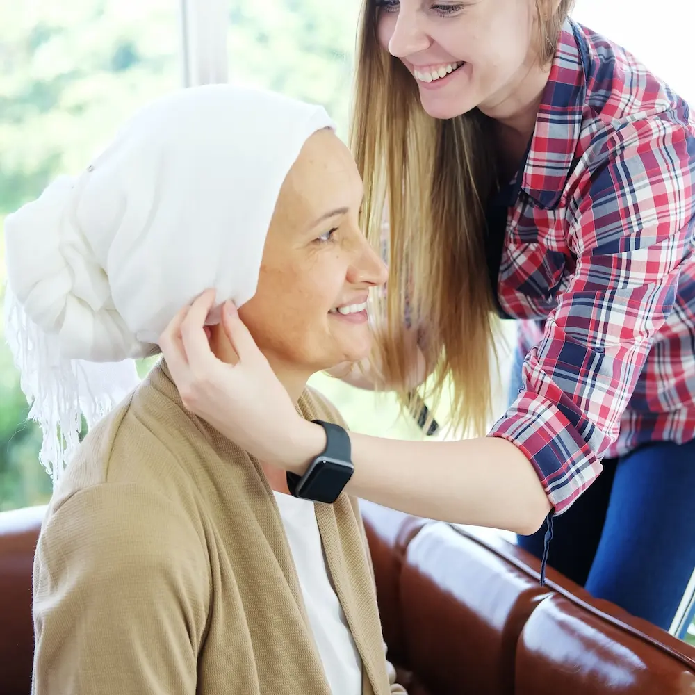 Smiling Caucasian young daughter is hugging and caring her Elderly Mother in white headscarf after chemotherapy.